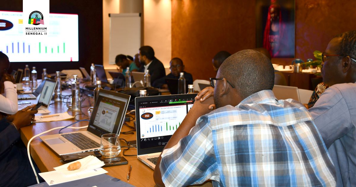 A member of the MCA-Senegal II ComVAD committee and other members review data on laptops at a conference table.