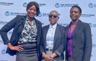 Three smartly dressed people standing next to each other in front of a banner with The World Bank written on it