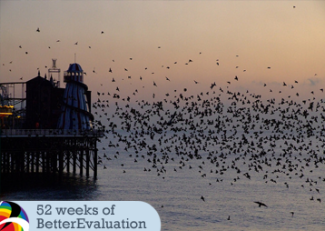 a flock of birds flies over a body of water by a pier